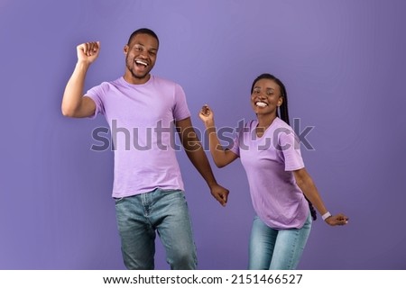 Having Fun. Portarit of excited young black couple dancing fooling around. Emotional happy guy and lady with afro braids enjoying favorite music together on purple violet studio background