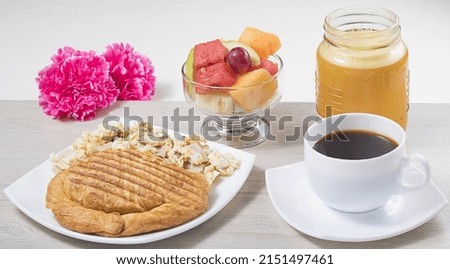 A closeup of a breakfast with sandwich and scrambled eggs, with fruits and coffee