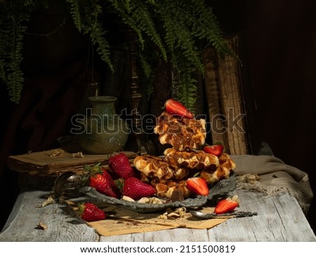 Viennese waffles with chocolate icing with ripe large strawberries on a vintage tray, on a light wooden table against the background of old books and fern twigs