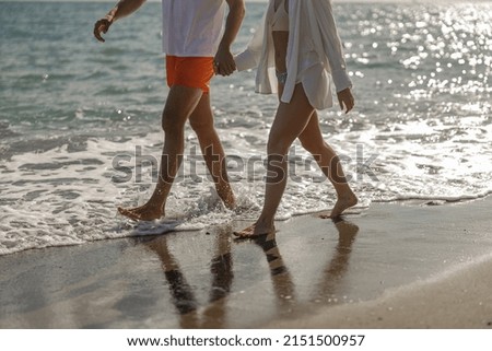 Cropped shot of young couple walking through waves on beach holiday