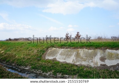 A beautiful landscape view of water channel by green hills with grass against a blue sky in San Giorgio di Piano in Italy