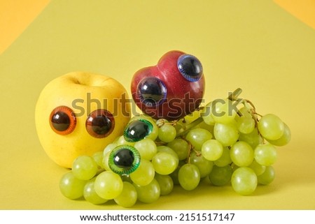 plum, apple and bunch of grapes with puppet eyes, prank concept, green background, april 1 prank, cute fruit faces