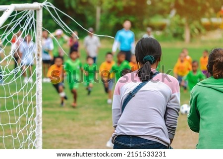Back view of Moms watch and cheering their sons playing football in school tournament on sideline. Sport, outdoor active,  Spectator watching soccer game. Parents care and encourage their children. Royalty-Free Stock Photo #2151533231