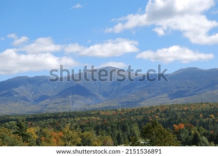 A horizontal shot of a white mountains on a background of a forest in autumn