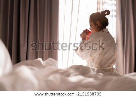 Cheerful tender asain adult female in white casual cloth sitting with cup of coffee on bed and having happiness cheerful smiling enjoy freshness while enjoying morning in bedroom at home or hotel