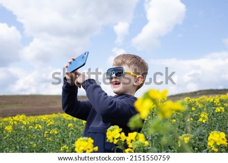 The boy takes pictures of the canola summer landscape on a smartphone. Children using technology.
