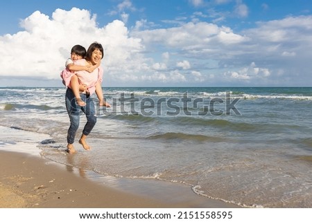 happy mother carrying her son on back and running on the beach