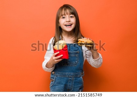 Portrait of a happy little girl about to eat a hamburger with some french fries in a studio and looking happy