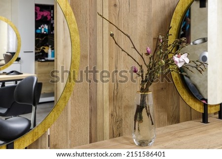 Pink magnolia flowers on branches  in glass vase on wooden work desk between two mirrors in hair salon. Interior decoration of beauty salon
