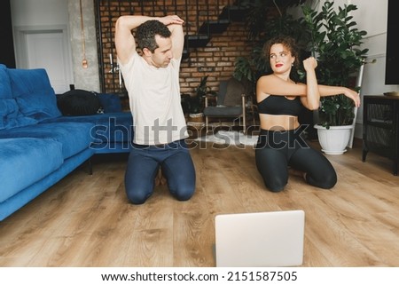 Young Caucasian sporty couple watching live or video tutorial practice sport lesson at home together. Healthy man and woman stretching and balancing body on floor. Sport lifestyle. High quality photo