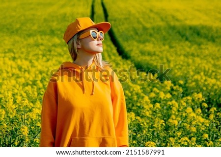 Stylish woman in yellow hoodie, cap and sunglasses in rapeseed field Royalty-Free Stock Photo #2151587991