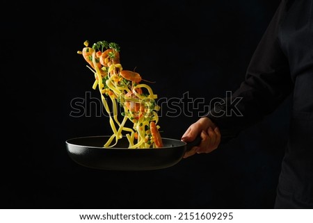 Italian pasta with greens and shrimps in a pan in a frozen flight on a black background. Sea food. Restaurant, hotel, banquet, home cooking. Healthy vegetarian food, healthy lifestyle. Royalty-Free Stock Photo #2151609295
