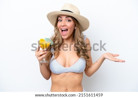 Young woman holding cocktail and wearing a bikini isolated on white background with shocked facial expression