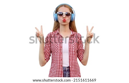 Portrait of young woman listening to music in headphones blowing her red lips isolated on white background