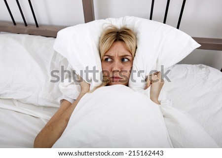 Young woman covering ears with pillow in bed