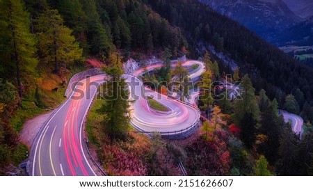 Maloja pass, Switzerland. A road with many curves among the forest. A blur of car lights. Landscape in evening time.  Royalty-Free Stock Photo #2151626607