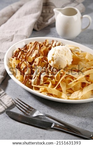 Crepes with ice cream on top with chocolate spread on white plate.  Sweet dessert.
