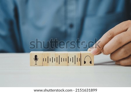 Hand put wooden cubes with Podcast mic and headphones symbol on table and copy space.Business concepts.