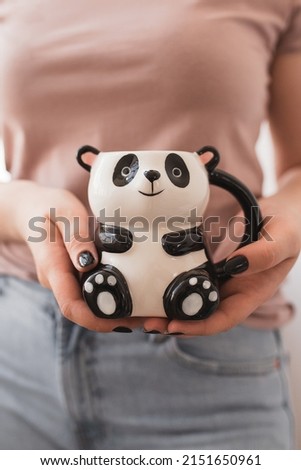 Mug in the shape of a panda for coffee and tea in the hands of a girl