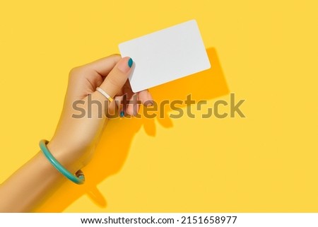 Beautiful groomed womans hand with fashionable holding business card on yellow background