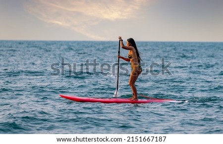 Beautiful woman wearing bikini  standing up paddle standing up paddling sup board in ocean sea is extreme water sport in holiday summer vacation. 