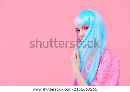 Hairstyling, hair dye. Portrait of a beautiful girl with colored purple-blue hair and bright pink makeup posing in pink dress on a pink background with copy space. Beauty, fashion. 