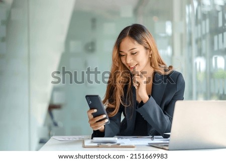 Happy young Asian business woman with a smile using smartphone at the office.