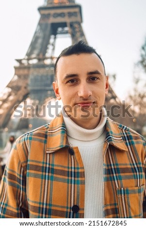 Guy tourist on the background of the Eiffel Tower posing. Male tourist laughs and smiles. Handsome brunette on a trip.