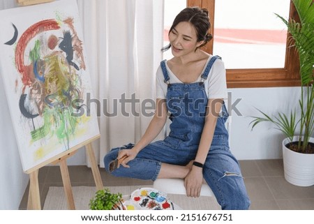 Creative of art concept, Young asian woman hold paint brush and happy to look on art masterpiece.