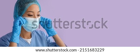 Asian nurse in medical mask on lilac background with space for text