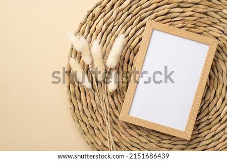 Top view photo of wooden photo frame white lagurus flowers and decorative placemat on isolated beige background with copyspace