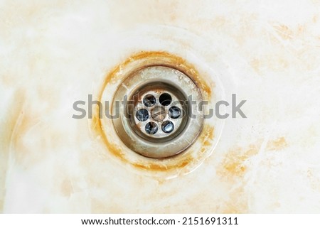 An old rusty bathtub with a metal drain hole. Dirty cracked unclean surface of the bath or sink with red rust stain, close-up. Corrosion, unsanitary concept. Royalty-Free Stock Photo #2151691311