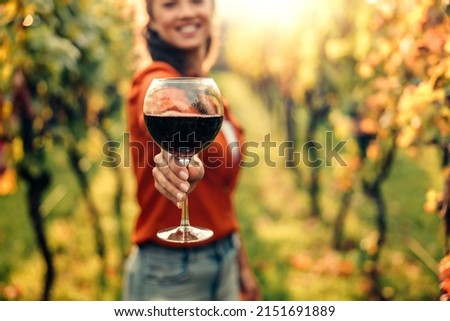 Woman tasting wine in vineyard. She is showing glass of wine to camera. Royalty-Free Stock Photo #2151691889