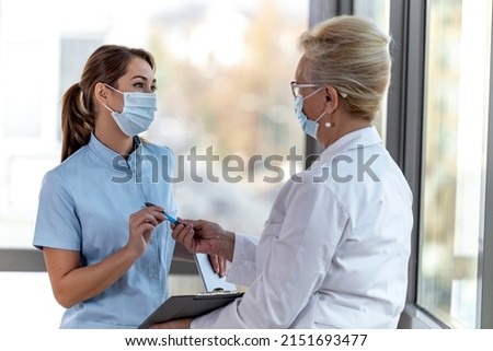 Two female doctors discussing while standing in office. Epidemic. Covid-19. Royalty-Free Stock Photo #2151693477