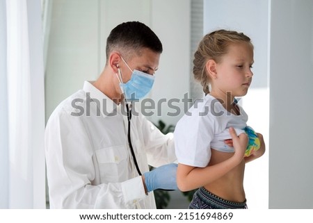 A doctor in a medical mask listens to the lungs of a child with a stethoscope. A doctor examines a little girl during an illness. Calling a doctor at home.