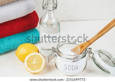 Baking soda in jar with a wooden spoon on top, vinegar, cut lemon, folded towel on a white background. The concept of organic removing stains on clothes. High quality photo Royalty-Free Stock Photo #2151699773