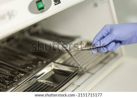 Close-up hands with gloves in the places medical autoclave for sterilising surgical and dental instruments. Dentist assistant's hands get out sterilizing medical instruments from autoclave.
