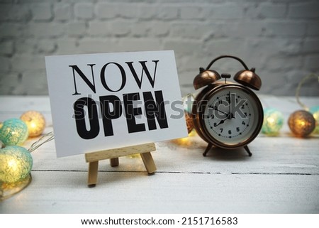 Now Open text and alarm clock on white brick wall and wooden background Royalty-Free Stock Photo #2151716583