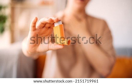 A girl suffering from an asthma attack due to allergies shows an inhaler while sitting on the sofa in the living room of the house. the concept of combating allergies. selective focus. Royalty-Free Stock Photo #2151719961
