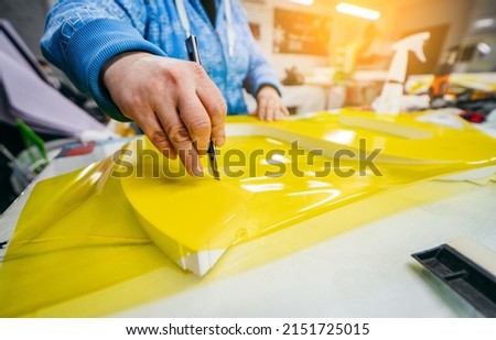 Applying colored yellow membrane to a surface of plastic 3d letter of signboard. worker's hands close up	
