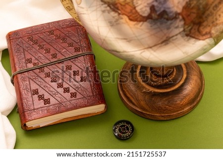 Leather notebook with small compass and part of a globe on a green background. Concept of travel, adventure and travel lifestyle.
