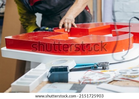 Young worker with a drill in his hand collects an advertising sign	
