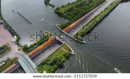 Aerial drone view of modern aqueduct or water bridge is constructed to convey watercourses across gaps showing a sailboat moving over the infrastructure and vehicles cars driving under 4k quality Royalty-Free Stock Photo #2151727039