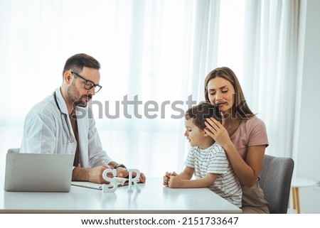 Smiling male pediatrician in white medical uniform holding clipboard, listening to young mother with kid son at checkup meeting, professional children doctor consultation, healthcare concept.