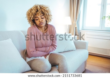 Cropped shot of an attractive young woman lying on her sofa alone and suffering from period cramps at home. Ouch! My tummy! Woman with menstrual pain