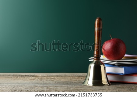 Golden school bell, apple and books on wooden table near green chalkboard. Space for text Royalty-Free Stock Photo #2151733755