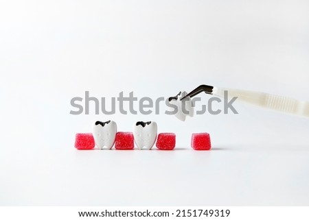 Cavities teeth between sweet sugar red jelly instead of gum Cavity and tooth decay pinching by clamp make a hole on white background, left a long time, too late to see dentist may have to lose teeth