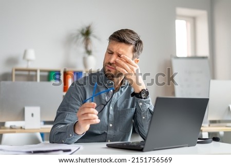 Tired mature man feeling pain eye strain, rubbing dry irritated eyes, fatigued from computer work, suffering from headache, bad vision sight problem sitting in office Royalty-Free Stock Photo #2151756569