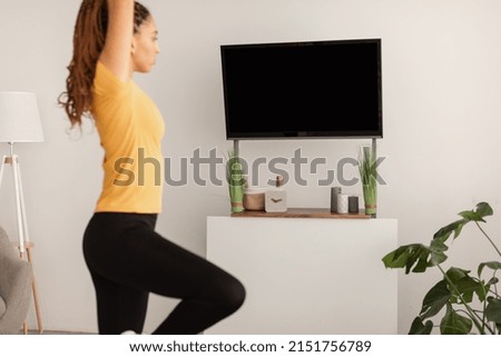 Cropped Shot Of Sporty Black Lady Doing Yoga Standing With Raised Hands Near TV Empty Screen At Home. Fitness And Sport Concept. Side View, Selective Focus On Plasma Set.