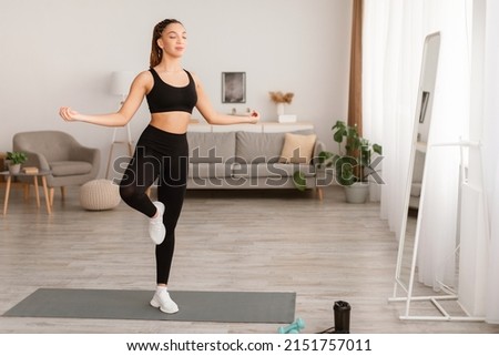 Sporty Black Lady Standing In Balance Yoga Pose On One Leg At Home. Peaceful Fit Woman Meditating With Eyes Closed In Living Room. Mediation, Relaxation And Mindfulness. Full Length